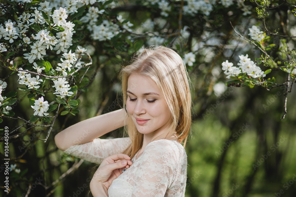 Naklejka premium Young beautiful blonde woman in blooming garden. Delicate girl enjoys spring nature