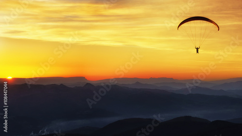Paraglide silhouette over mountains at sunset
