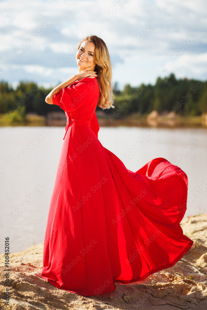 Gorgeous red head young woman in long red dress on a background of a lake. Sandy canyon. Fashion style Gorgeous red head young woman in long red dress on a background of a lake. Sandy canyon. Fashion style