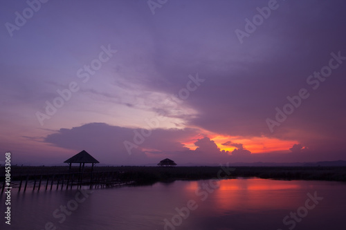 Wooden bridge and lagoon with sunset backdrop.