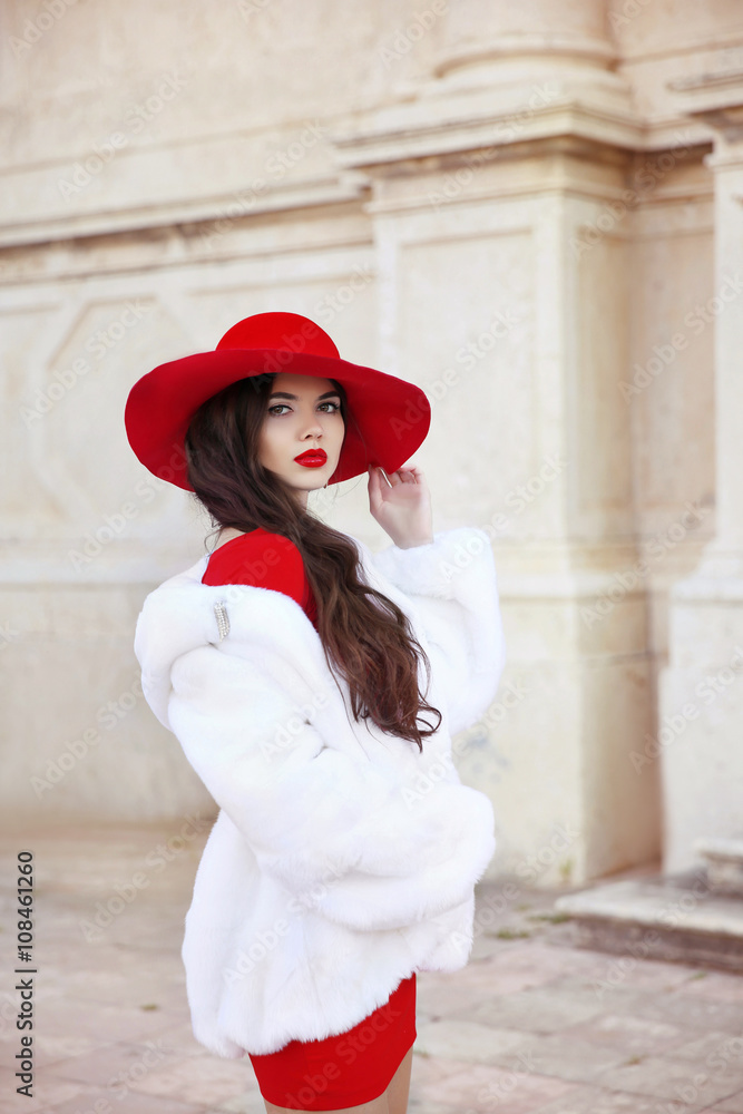 Fashion woman in red hat and dress wearing white fur coat. Elega