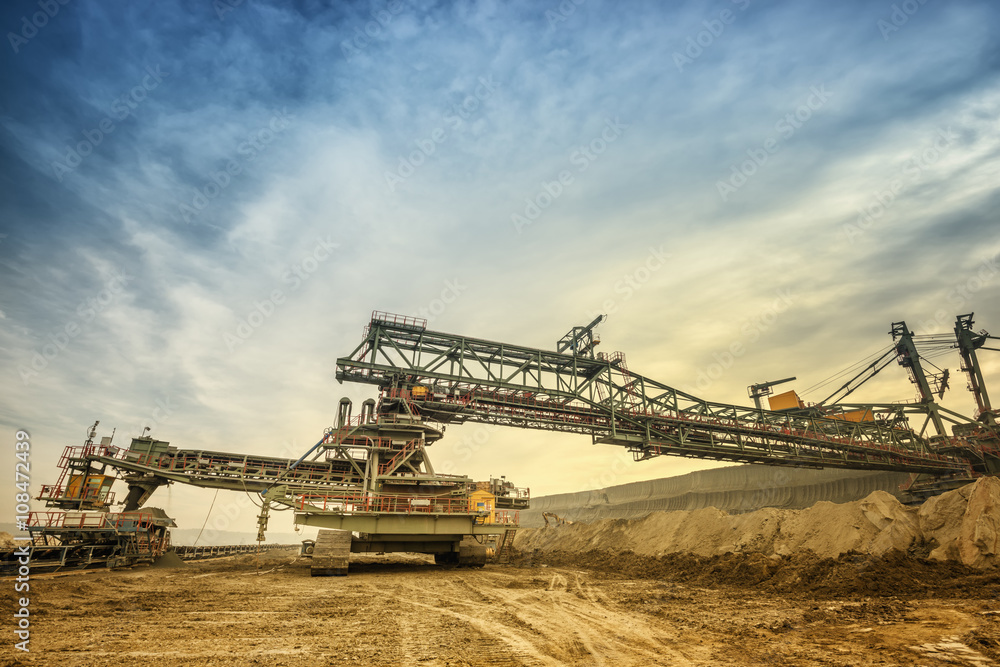 One side of huge mining drill machine connected to transportation facility. Photographed from a ground with wide angle lens. Dramatic and colorful sky in background. One side of huge mining drill machine connected to transportation facility. Photographed from a ground with wide angle lens. Dramatic and colorful sky in background.