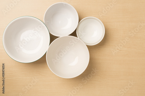 Four empty bowls on light wood background  top view