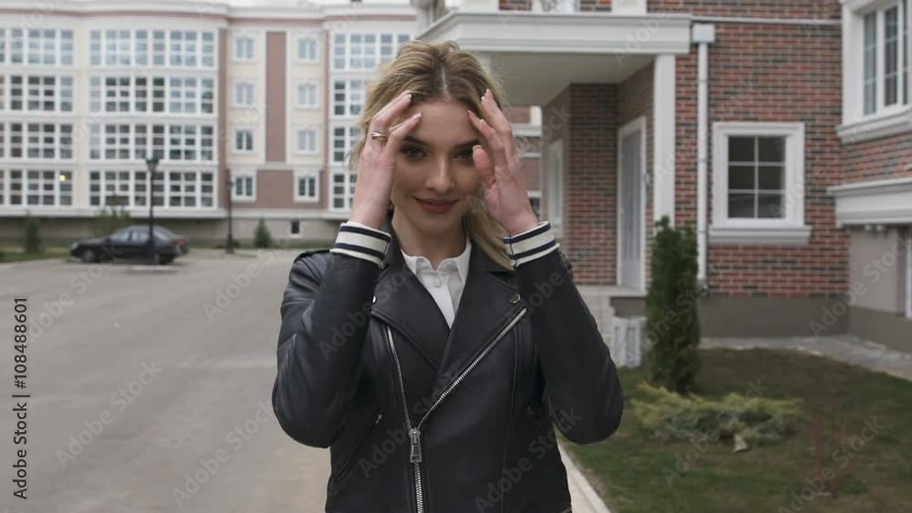Young woman walking on the street. Blonde turns flirting gaze with the viewer. Black leather jacket Young woman walking on the street. Blonde turns flirting gaze with the viewer. Black leather jacket