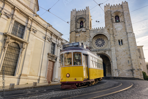 A famous yellow tram 28 passing in front of Santa Maria cathedral, Lisbon, Portugal