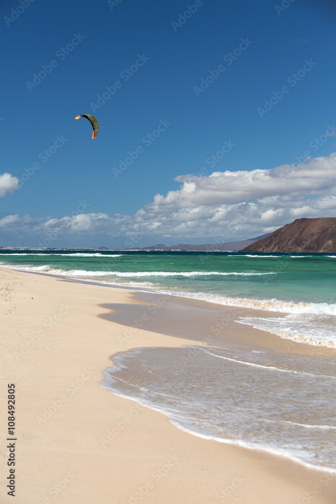  Unknown kitesurfer surfing on a flat azure water of Atlantic ocean in Corralejo, Fuerteventura, Canary islands, Spain