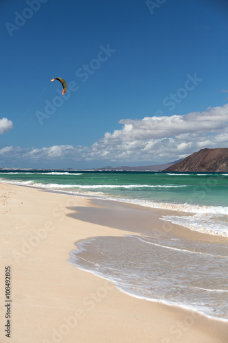  Unknown kitesurfer surfing on a flat azure water of Atlantic ocean in Corralejo, Fuerteventura, Canary islands, Spain