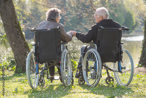 Elderly couple in wheelchairs, holding hands