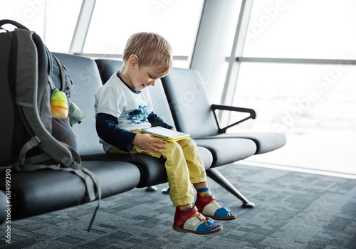 Little boy sitting in an airport departure hall and playing on his tablet 