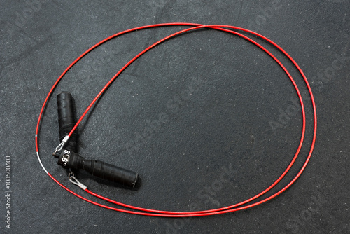 Photography Red jump rope with black handles on a black gym floor