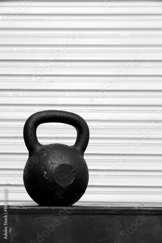 Black kettle bell on a black jump box  against a white roll-up door  