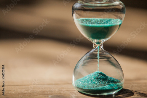 Sand running through the bulbs of an hourglass measuring the passing time in a countdown to a deadline, on a dark background with copy space.