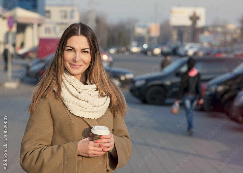 Fototapeta premium Beautiful brunette woman holding a bag and cup of hot tea or coffee, standing in the street