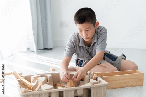 Asian boy playing a Structure from Wooden Building Blocks with b