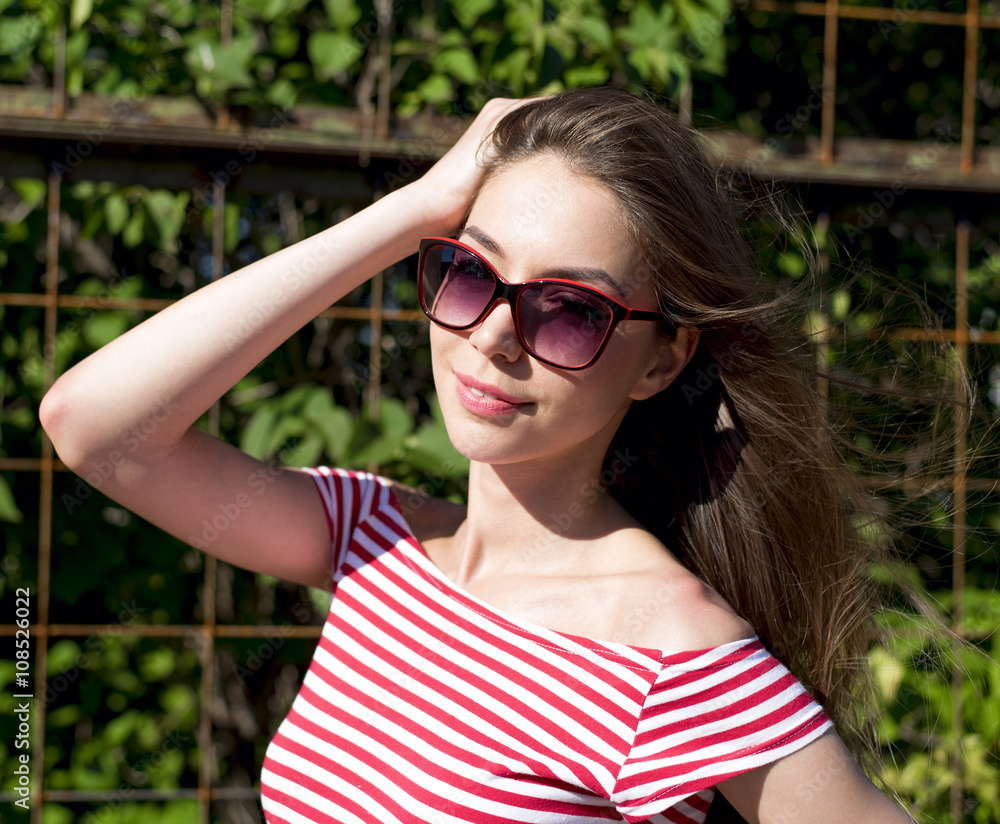 Beautiful girl in a bright red T-shirt, fashion lifestyle, posing against the backdrop of fence with green leaves Beautiful girl in a bright red T-shirt, fashion lifestyle, posing against the backdrop of fence with green leaves