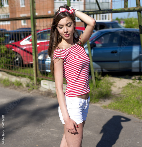 Beautiful girl outdoors on the playground, resting in a bright red T-shirt white shorts