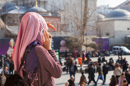 Young woman stands in front of the New Mosque ( Yeni Cami ) and speaks on the mobile phone