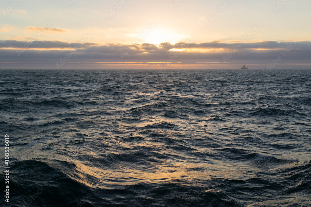 Sunset in the sea with cargo ship on horizon.