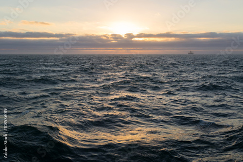 Sunset in the sea with cargo ship on horizon.