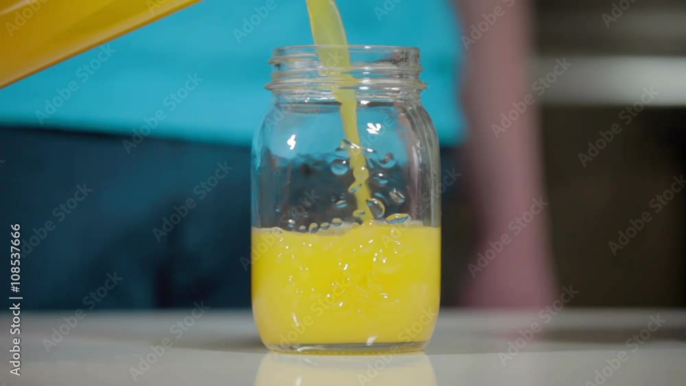 Pouring orange juice from bottle to glass jar Pouring orange juice from bottle to glass jar