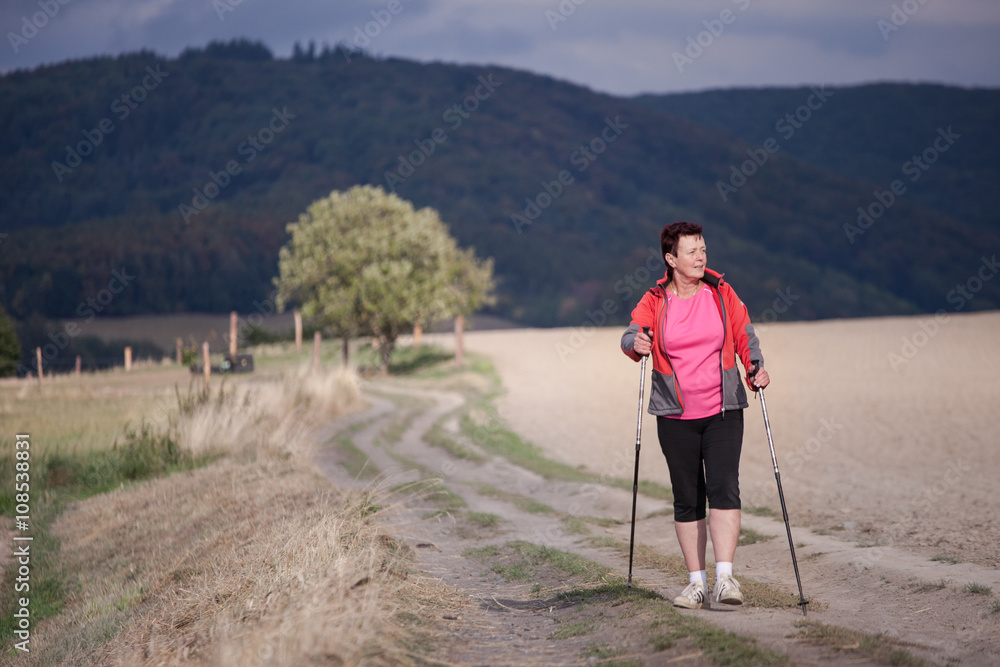 Middle aged woman nordic walking, enjoying the outdoors, the fresh air, getting the necessary exercise