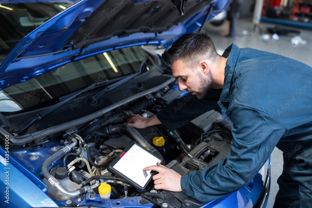 Mechanic using a diagnostic tool while examining car engine at the repair garage Mechanic using a diagnostic tool while examining car engine at the repair garage