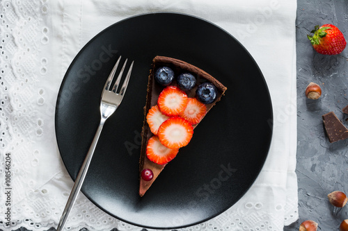 Piece of chocolate pie (cake, tart) decorated with fresh fruits and berries on black plate. Top view photo