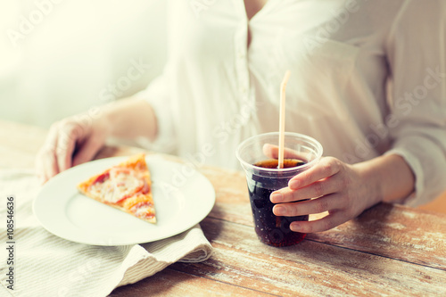 Midsection of woman with pizza slice and cola soda drink