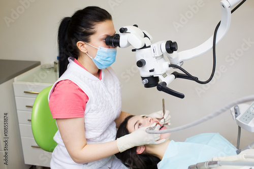 professional dentist examination patient with microscope at the office.Dentist looking through microscope at surgery office