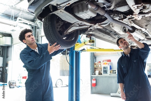 Mechanic fixing a wheel while a colleague examining car