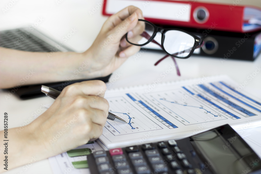 Businesswoman analyzing graphic and using calculator in the office Businesswoman analyzing graphic and using calculator in the office
