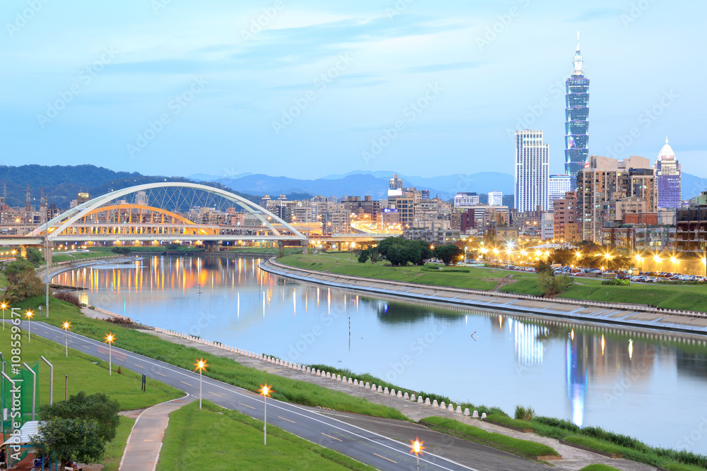 Fototapeta premium Nocna sceneria Taipei City z pięknymi odbiciami drapaczy chmur i mostów na gładkiej wodzie nad rzeką o zmierzchu ~ Pejzaż Tajpej 101, rzeka Keelung, dzielnica Xinyi i centrum o zmierzchu
