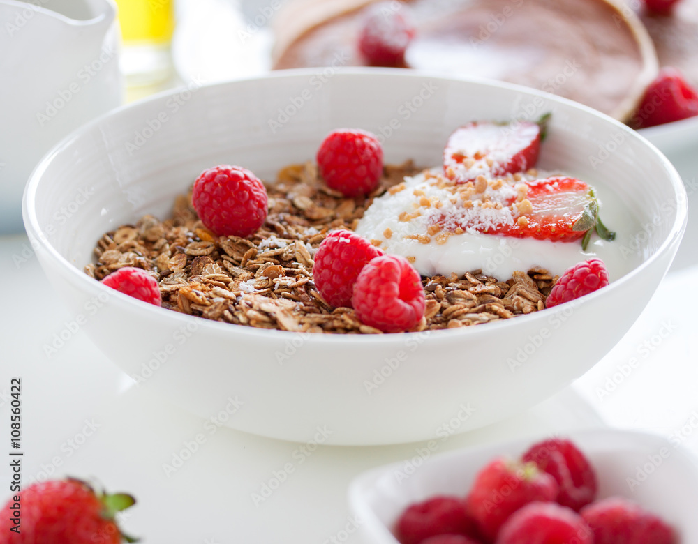 Homemade oat meal granola or muesli with fresh summer fruits – raspberry and strawberry with yogurt in a white bowl on a table for breakfast, closeup, selective focus. Homemade oat meal granola or muesli with fresh summer fruits – raspberry and strawberry with yogurt in a white bowl on a table for breakfast, closeup, selective focus.