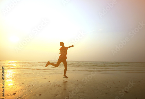 Silhouette young girl jumping with hands up on the beach