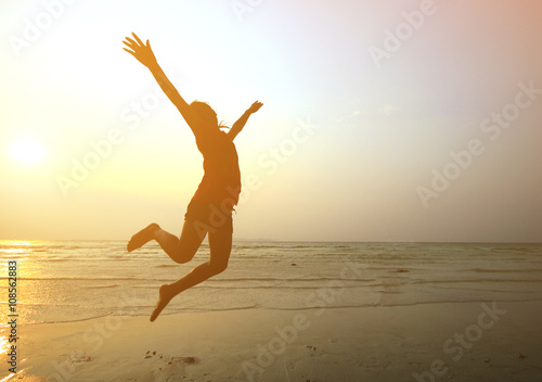 Silhouette young girl jumping with hands up on the beach at th