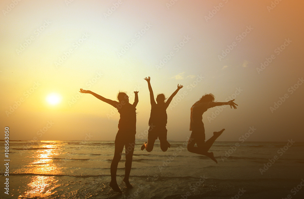 Fototapeta premium Silhouette of three young girls jumping with hands up on the be
