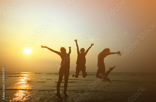 Silhouette of three young girls  jumping with hands up on the be