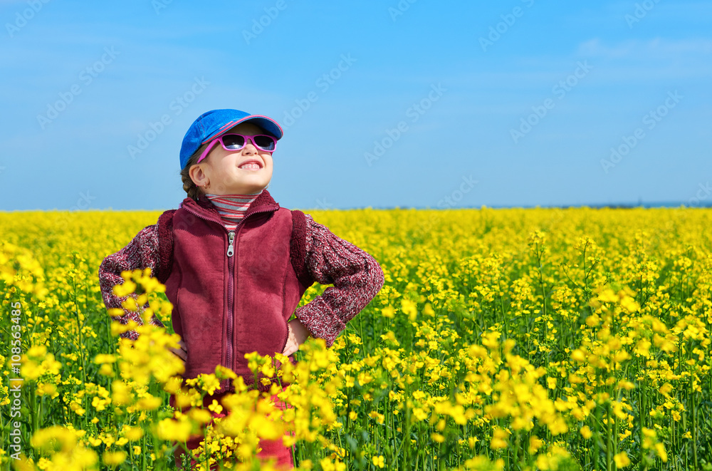 Fototapeta premium girl child in rapeseed field with bright yellow flowers, spring landscape