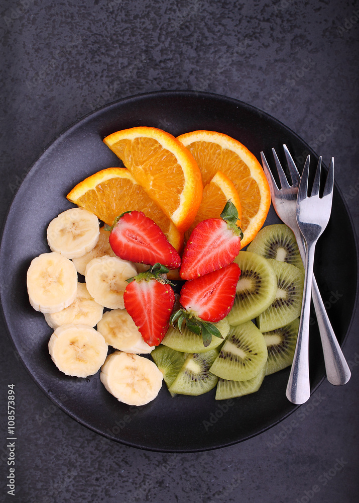 sliced fruit (strawberries, kiwi, orange, banana) on a black plate sliced fruit (strawberries, kiwi, orange, banana) on a black plate