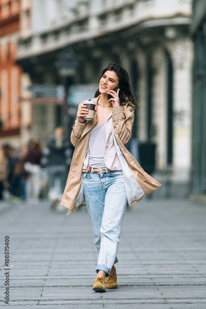 Young beautiful woman with coffee to go walking at the street and talking on mobile phone
