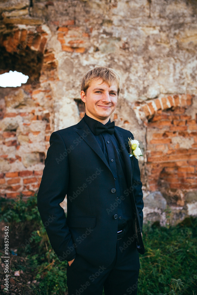 Handsome rich confident groom posing near wall Handsome rich confident groom posing near wall