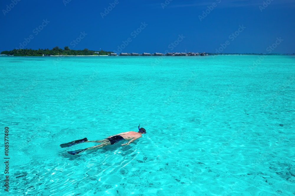 Naklejka premium Young man snorkeling in tropical lagoon with over water bungalows