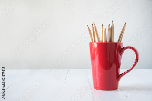 pencils in red cup on white wooden table