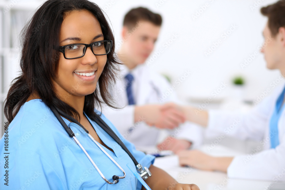 Female african american medical doctor with colleagues in background Female african american medical doctor with colleagues in background