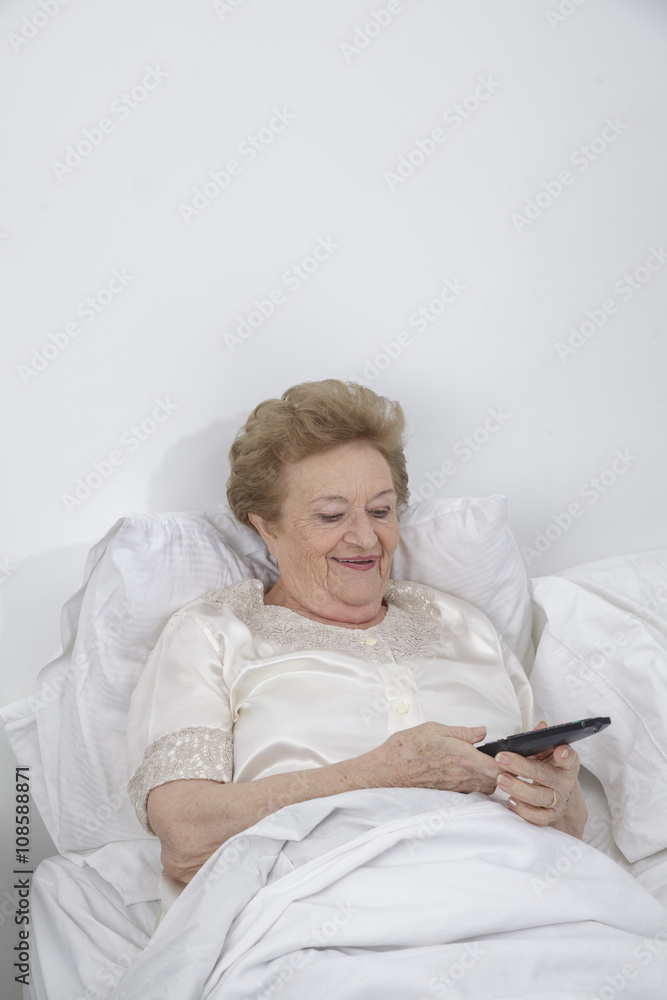senior woman lying in bed with tv remote senior woman lying in bed with tv remote