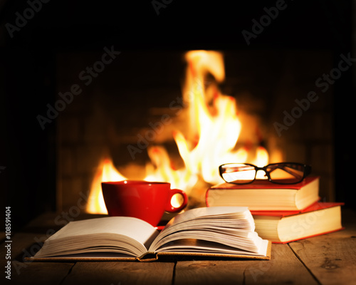 Red cup and old books on wooden table near fireplace.