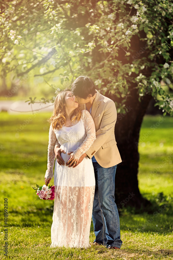 Fototapeta premium Expecting mom and dad kissing under flowering tree