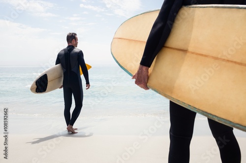 Rear view of man walking with surfboard on the beach