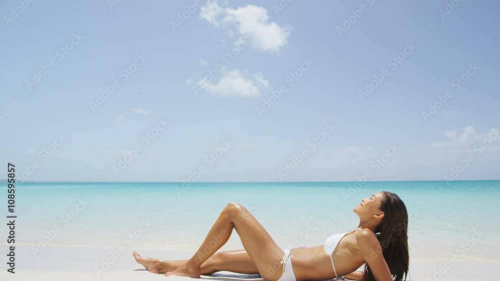 Suntan woman relaxing on summer beach vacation. Sexy young ethnic Asian Caucasian adult in bikini sitting down on perfect white sand with sky copyspace for tropical travel destination concepts. Suntan woman relaxing on summer beach vacation. Sexy young ethnic Asian Caucasian adult in bikini sitting down on perfect white sand with sky copyspace for tropical travel destination concepts.