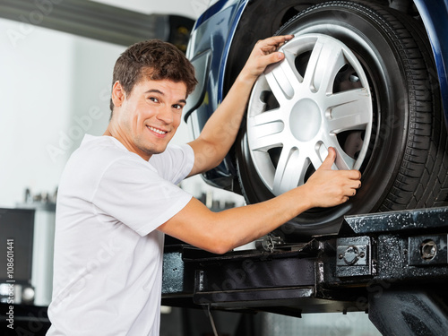 Happy Mechanic Fixing Hubcap To Car Tire photo